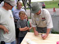 Michael Johnson demonstrates how to clean a trout to a couple successful anglers at the EAFB Party at the lake while their proud parents look on.